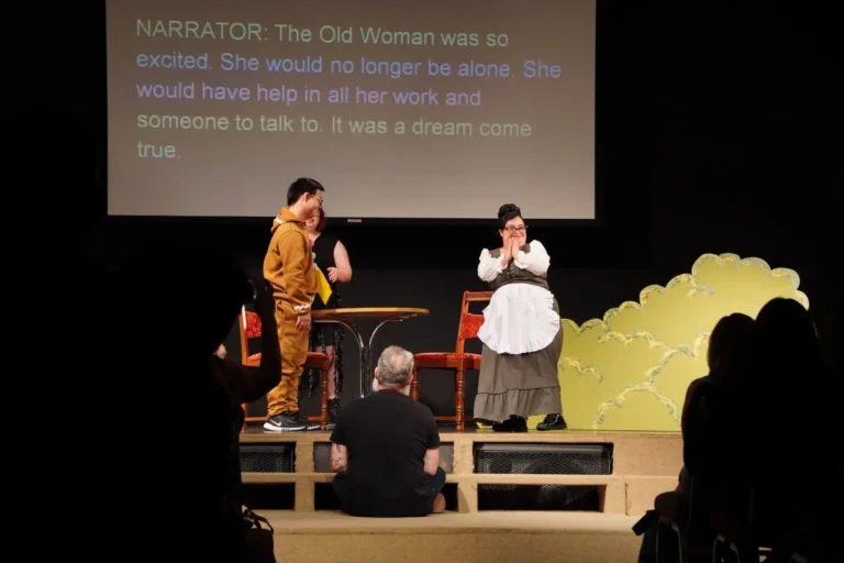 a woman in a white apron on a stage with a man in a chair
